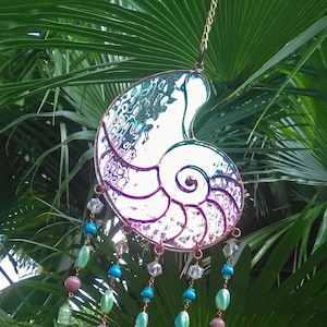 May include: A stained glass nautilus shell wind chime with iridescent purple, blue, and green colors. The shell is suspended from a chain with beads and crystals hanging from the bottom.