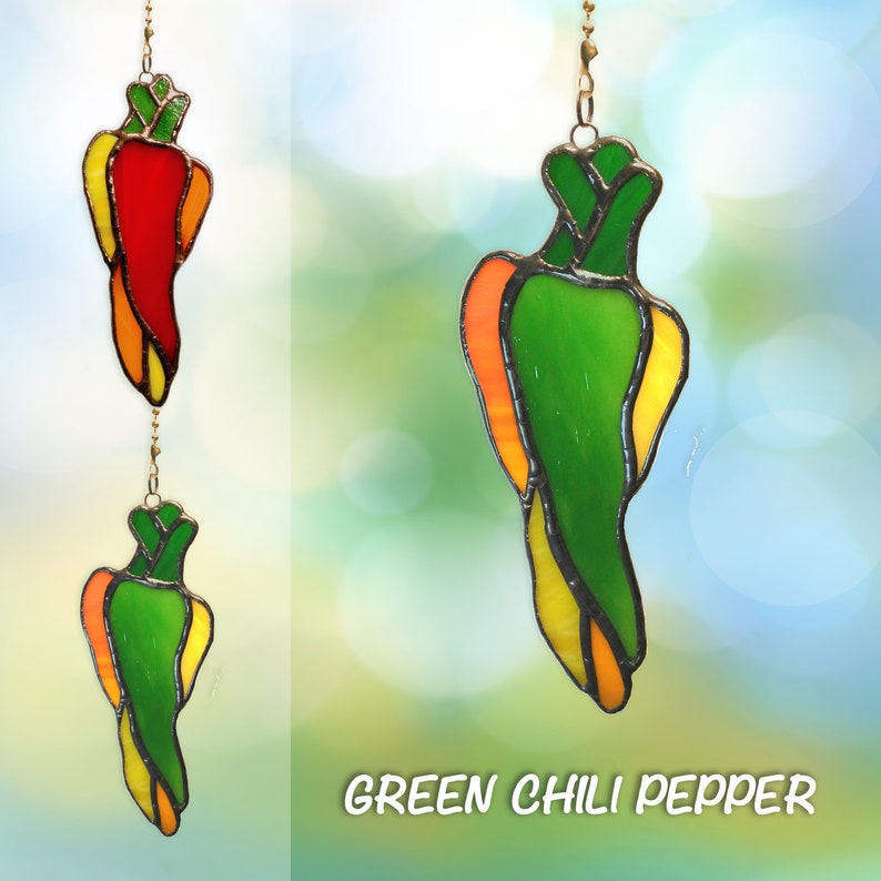 May include: A stained glass green chili pepper hanging ornament with yellow and orange accents. The ornament is suspended from a gold chain.