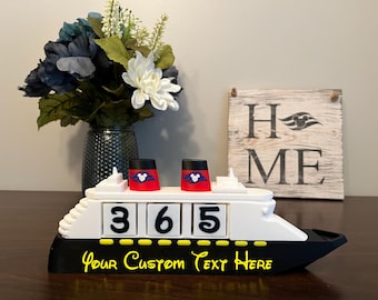May include: A white and black cruise ship countdown calendar featuring two red smokestacks with white Mickey Mouse icons. The ship displays the number 365 on white blocks and includes the yellow text Your Custom Text Here on the black hull.