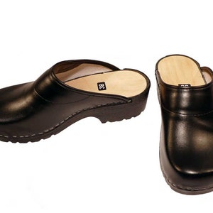 May include: A pair of black leather clogs with wooden soles. The clogs have a closed toe and a back strap. The size 38 is printed on the insole.