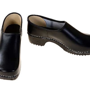 Könnte beinhalten: Ein Paar schwarze Lederschuhe mit Holzsohle. Die Clogs haben eine geschlossene Spitze und ein schlichtes Design.