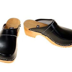 May include: A pair of black leather clogs with wooden soles. The clogs have a white stitching detail around the edges and a white strap across the top.
