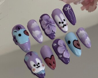Puede incluir: Conjunto de diez uñas postizas de color morado y azul con varios diseños, incluyendo nubes, flores y personajes de dibujos animados.
