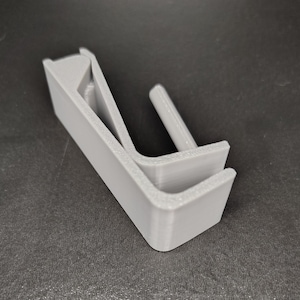 May include: A gray plastic hook with a curved design. The hook is made of two pieces that fit together.