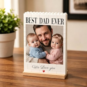 Peut inclure: Cadre photo blanc en forme de briques avec l'inscription "BEST DAD EVER" et "We Love you". Il contient une photo d'un homme et de deux bébés. Le cadre repose sur une base en bois.