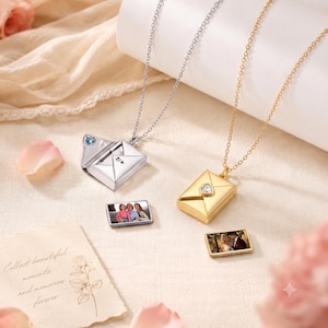 May include: Two envelope-shaped locket necklaces, one silver-toned with a blue stone and one gold-toned with a heart-shaped stone. Each necklace includes a small rectangular insert featuring a printed photograph of people.