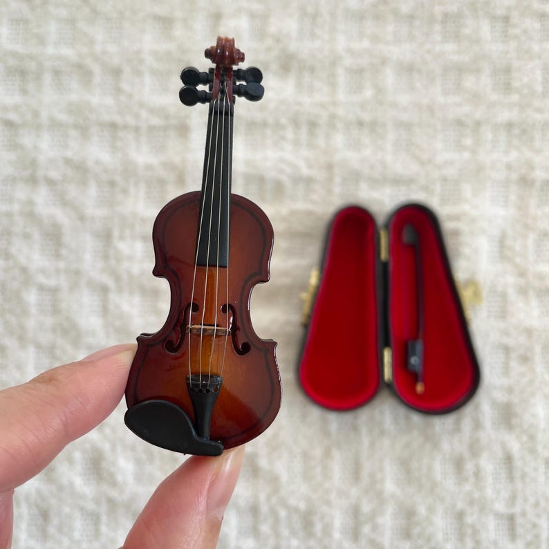 Puede incluir: Un viol&iacute;n en miniatura con un cuerpo de madera marr&oacute;n y clavijas negras. El viol&iacute;n est&aacute; en una caja de terciopelo rojo.