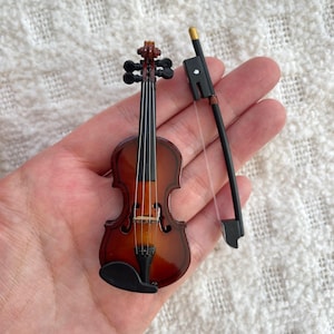 Puede incluir: Un viol&iacute;n de madera en miniatura con un acabado marr&oacute;n y cuerdas negras. Viene con un arco negro.