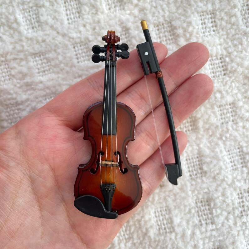 Puede incluir: Un viol&iacute;n de madera en miniatura con un acabado marr&oacute;n y cuerdas negras. Viene con un arco negro.
