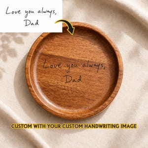 以下が含まれることがあります： 中央に「Love you always, Dad」と刻印された円形の茶色の木製トレイ。トレイは滑らかで光沢のある仕上げで、縁が盛り上がっています。上部の白いカードには同じテキストが表示され、黄色い矢印がトレイを指しています。