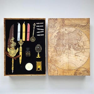 May include: An antique-style calligraphy set in a decorative box. The set includes a feather quill pen, ink bottle, wax seals, a wax melting spoon, and various pen nibs. The box lid features a vintage world map design.