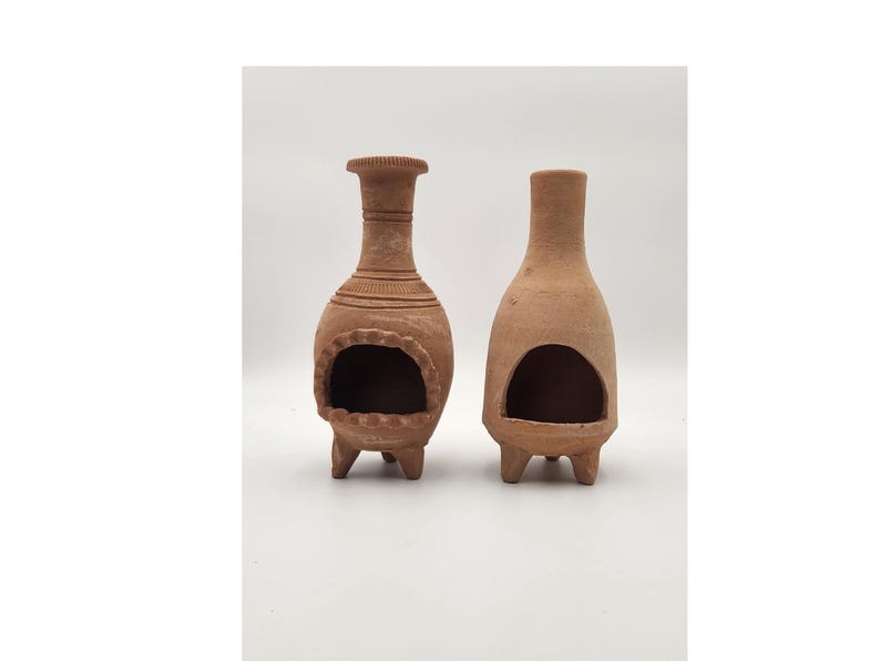 Pu&ograve; includere: Due bruciatori di incenso in terracotta con un'apertura rotonda e tre gambe. I bruciatori sono di colore marrone e hanno un aspetto rustico.