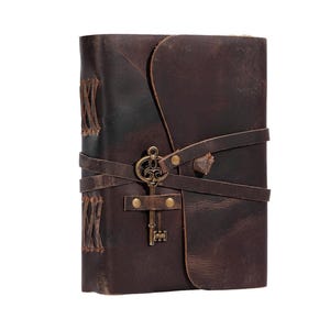 May include: A brown leather journal with a key-shaped metal clasp. The journal has a distressed look and is secured with leather straps.
