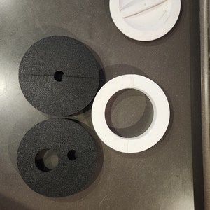May include: Four round, flat, foam circles. Two are black with a hole in the center. One black circle has a smaller hole inside the larger hole. The other two circles are white with a hole in the center. One white circle has a slit across the center.