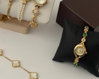 Reloj de pulsera dorado de inspiración vintage con detalles de piedra verde y cristal.