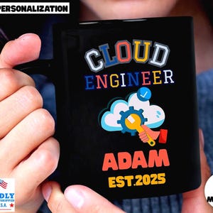 May include: A black ceramic mug featuring the text CLOUD ENGINEER in blue and white, a graphic of a cloud with a blue gear and a yellow wrench, the name ADAM in orange, and the text EST. 2025 in yellow. The design is printed on the front surface.