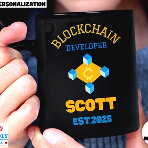May include: Black coffee mug with the words "BLOCKCHAIN DEVELOPER" in yellow and blue. The mug features a graphic of a yellow square with a crypto symbol and blue cubes. The name "SCOTT" and the year "EST.2025" are also printed on the mug.