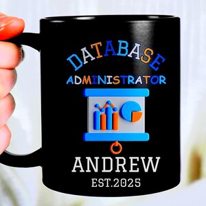 May include: Black ceramic mug with the words "DATABASE ADMINISTRATOR" in blue and orange lettering. Below the text is a graphic of a data chart. The name "ANDREW" and the year "EST.2025" are printed in white.