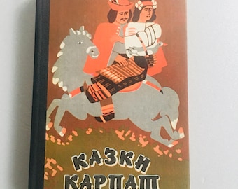 Puede incluir: Una portada de libro vintage con fondo marrón y una ilustración colorida de una pareja montando a caballo. El texto de la portada dice "КАЗКИ КАРПАТ".