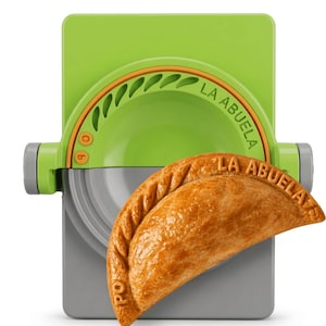 May include: A lime green and grey plastic empanada press featuring the text LA ABUELA embossed on the curved edge. A golden-brown, crescent-shaped empanada with a crimped edge and the text LA ABUELA embossed on its surface rests on the press.