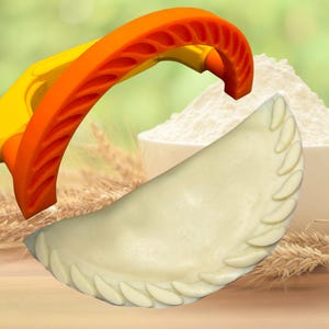 Puede incluir: Prensa de repostería de plástico naranja y amarillo con un borde decorativo. La prensa se utiliza para crear un borde decorativo en los pasteles. Se muestra un pastel blanco con un borde decorativo en primer plano.