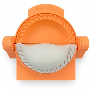 Puede incluir: Un molde para empanadillas naranja con la marca "SAMPAOLI" impresa en la parte superior. La herramienta tiene un diseño semicircular con un borde ondulado y contiene una empanadilla blanca.