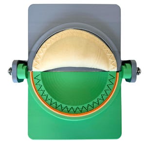 Puede incluir: Una prensa de cocina para empanadillas con una placa superior gris y una placa inferior verde con un molde circular. El dispositivo incluye un mecanismo de bisagra con soportes laterales verdes y pasadores metálicos, sosteniendo una masa.