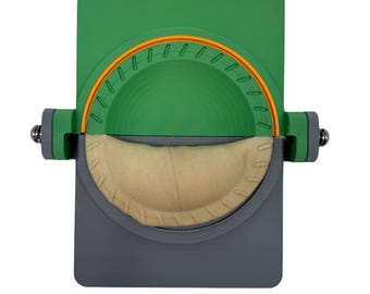 Puede incluir: Una prensa de pastelería manual verde y gris con un pastel beige en su interior. La prensa tiene una abertura circular con un borde naranja.