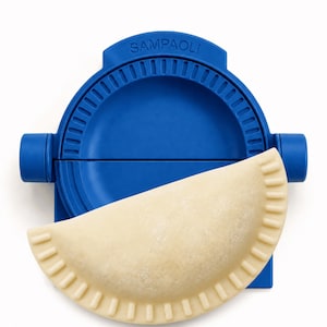 May include: A blue plastic ravioli maker with the word "SAMPAOLI" printed on the top. A filled, uncooked ravioli is placed in the maker. The ravioli maker has a semi-circular shape with a crimped edge.