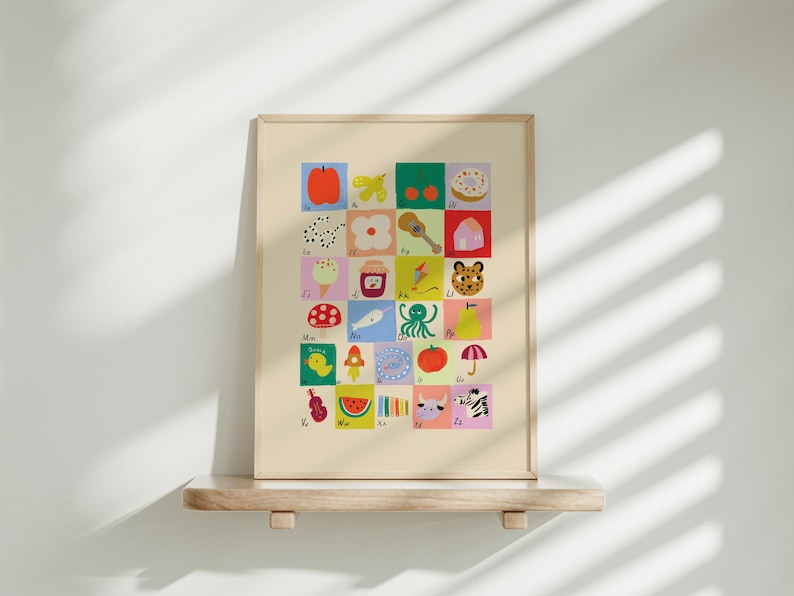 May include: A framed alphabet art print featuring colorful illustrations of various objects, each representing a letter. The artwork includes images of an apple, butterfly, donut, ice cream, and more. The print is displayed on a wooden shelf against a white wall.