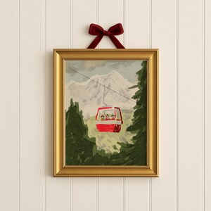 May include: A framed print featuring a red ski lift ascending a mountain, surrounded by green trees. The artwork is in a gold frame and is suspended by a red velvet bow. The painting depicts a winter scene.
