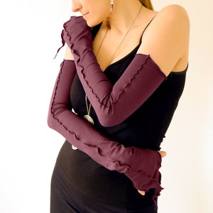 May include: A pair of long, burgundy arm warmers with a scalloped edge. The arm warmers are made of a soft, stretchy fabric and are perfect for adding a touch of style to any outfit.