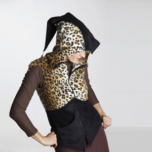 Puede incluir: Un chaleco de estampado de leopardo negro y marrón con una parte superior con capucha negra. El chaleco tiene una cremallera y un bolsillo en la parte delantera.