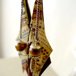 May include: A pair of dangle earrings with a geometric design. The earrings are made of leather with a brown and gold pattern. Each earring has a brown tiger's eye bead at the end.