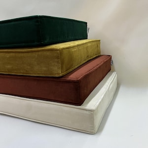 Könnte beinhalten: Ein Stapel von vier rechteckigen Kissen in verschiedenen Farben: Dunkelgrün, Senfgelb, Rost und Creme. Die Kissen haben eine weiche, samtige Textur und ein schlichtes, modernes Design, geeignet für die Inneneinrichtung.