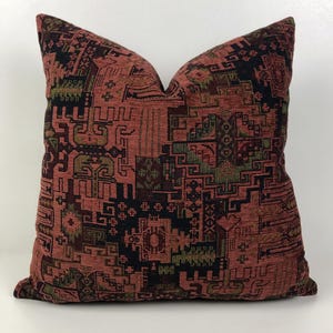 Op de afbeelding: Een rood, zwart en groen kussen met een geometrisch patroon.