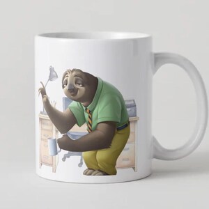 Op de afbeelding: Witte keramische mok met een cartoon luiaard karakter in een groen shirt en gele broek, met een kleine mok. De luiaard bevindt zich in een kantooromgeving met een bureau en een lamp. De mok heeft een wit handvat en een wit interieur.