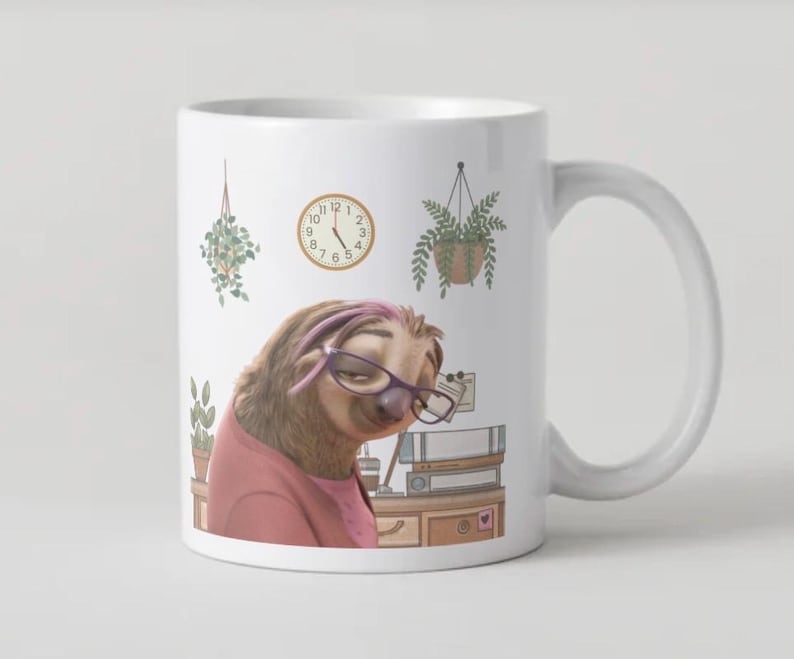 Op de afbeelding: Witte keramische mok met een cartoon luiaard met een bril en een roze shirt. De mok heeft een klok en hangende planten ontwerp. De luiaard wordt afgebeeld in een kantooromgeving.