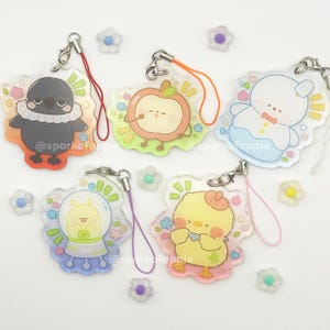 May include: Five acrylic charms with cartoon animal designs, including a crow, apple, bear, snail, and chick. Each charm has a silver clasp and a colored lanyard. The charms are surrounded by small flower-shaped decorations.