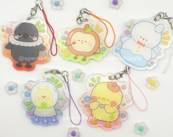 May include: Five acrylic charms with cartoon animal designs, including a crow, apple, bear, snail, and chick. Each charm has a silver clasp and a colored lanyard. The charms are surrounded by small flower-shaped decorations.