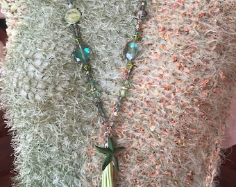 May include: A green and brown fuzzy sweater with a green beaded necklace featuring a starfish charm and a green tassel.