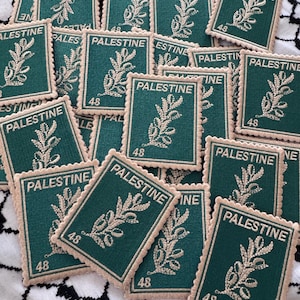 May include: A collection of embroidered patches with a postage stamp design. Each patch is dark green with the word "PALESTINE" and a sprig of leaves in beige. The number "48" is also visible on each patch.