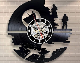 May include: Black vinyl record clock featuring Star Wars characters and a Death Star design. The clock has a white face with black numbers and a visible mechanical movement. The clock is mounted on a white brick wall.