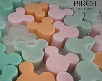 May include: Assortment of pastel-colored Mickey Mouse shaped soaps. The soaps are in shades of pink, green, orange, and white. The soaps are arranged in a random pattern. The text "BIRCH Bath & Body company" is visible in the top right corner of the image.