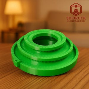 Könnte beinhalten: Ein leuchtend grünes, 3D-gedrucktes Objekt mit einem abgestuften, kreisförmigen Design. Es hat drei konzentrische Ringe, die jeweils etwas kleiner sind, wodurch ein gestuftes Aussehen entsteht. Der Text "3D DRUCK MANUFAKTUR" ist im Hintergrund sichtbar.