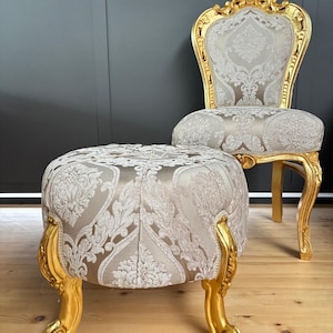May include: A gold-painted, ornate chair with a white and gold patterned fabric seat and back. Next to the chair is a matching footstool with the same fabric and gold painted legs.
