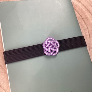 May include: A purple and white decorative knot tied with a black elastic band. The knot is a traditional Japanese design.