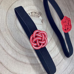 May include: Two black elastic hair ties with red and white knotted flower accents.