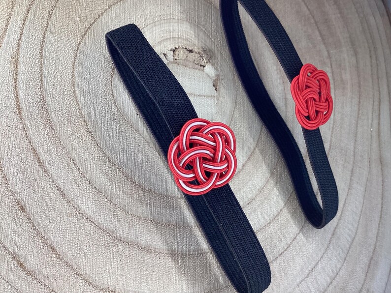 May include: Two black elastic hair ties with red and white knotted flower accents.