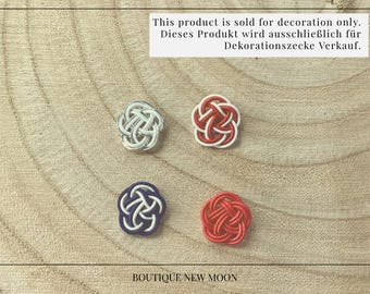 May include: Four decorative knots, each tied in a different color: white, blue, red, and silver. The knots are arranged in a square pattern on a wooden surface. The text "BOUTIQUE NEW MOON" is visible at the bottom of the image.
